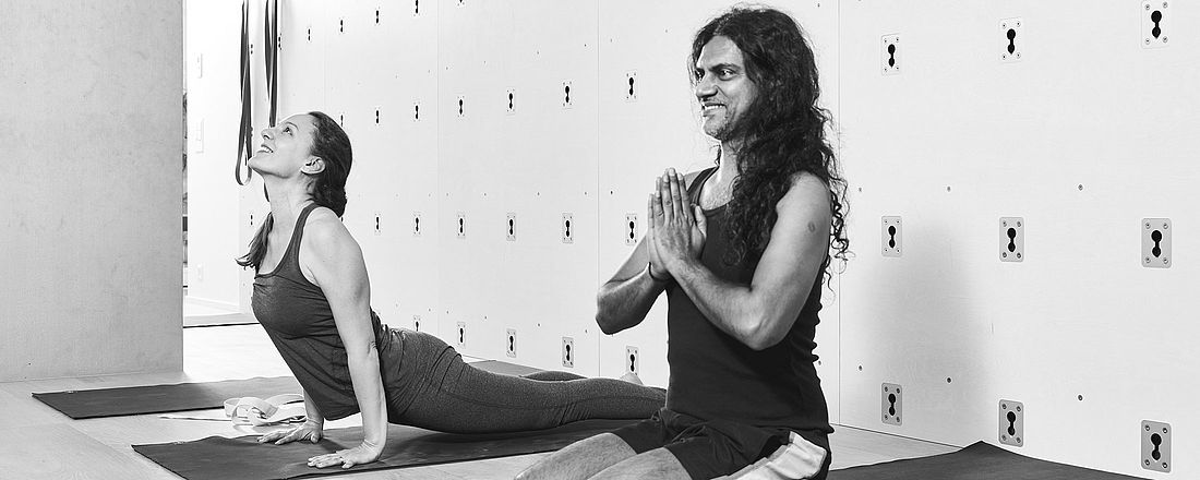 Tanja und Joey üben Yoga im Studio in Zürich. Man sieht die Yogawand im Hintergrund.  