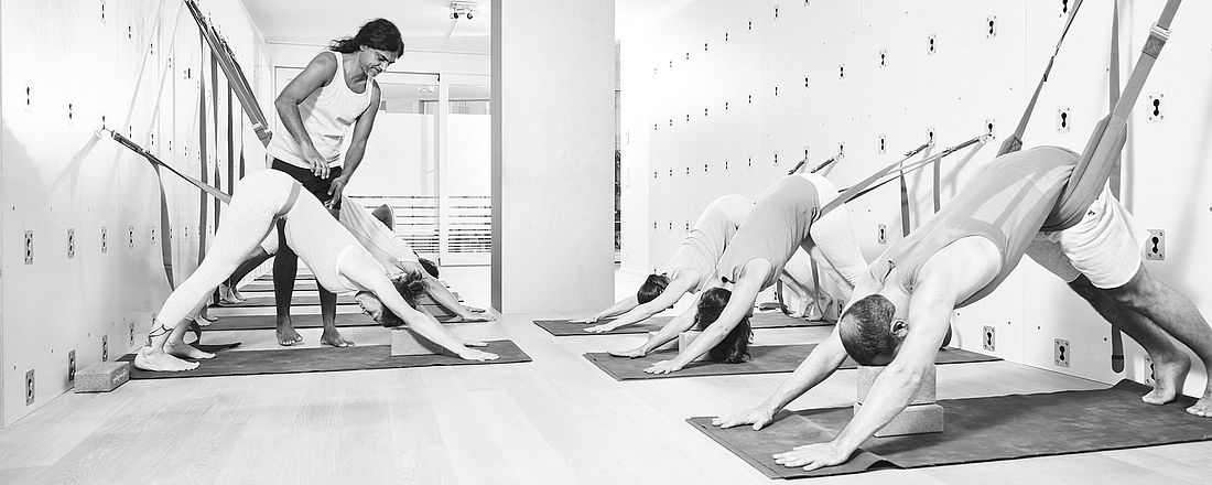 Joey von the yoga place in Zürich korrigiert eine Gruppe von Teilnehmer im Studio and der Yogawand. Man sieht auch Yogablöcke im Einsatz.