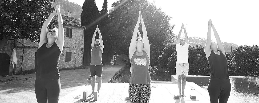 Teilnehmerinnen und Teilnehmer von the yoga place während einer Yogastunde in den Yogaferien. Alle strecken in die Arme in die Luft.